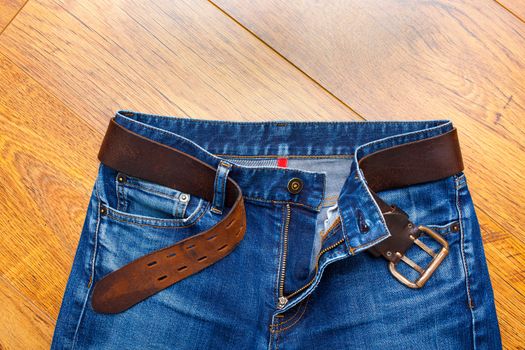 Aged jeans with a leather belt on a wooden surface