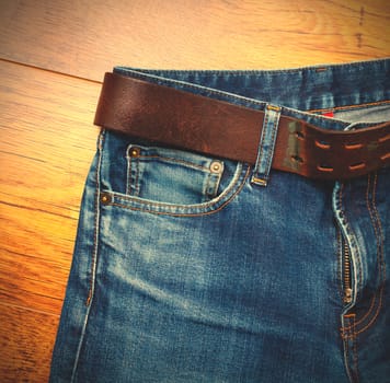 Aged blue jeans with a leather belt on wooden boards. copy space