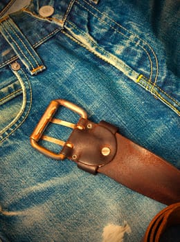 Vintage leather belt with a buckle lying on old jeans with a hole. instagram image retro style