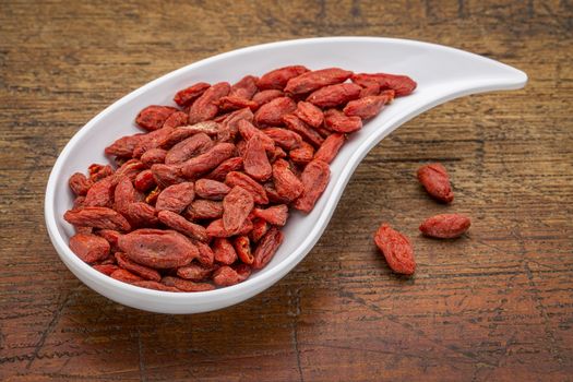 dried goji berries in a teardrop shaped bowl against rustic wood