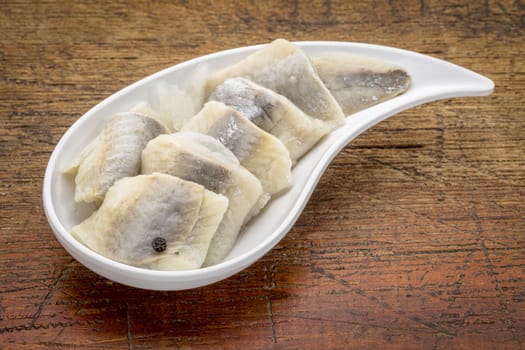 herring in wine sauce with  onion and spices - white teardrop shaped bowl against rustic wood wood