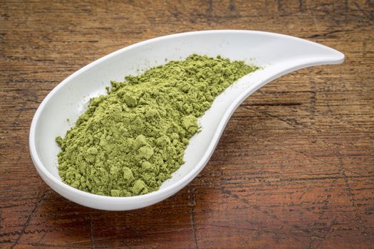 moringa leaf powder in a teardrop shaped bowl against rustic wood