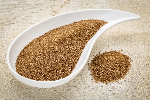 gluten free teff grain on a teardrop shaped bowl against white painted grunge wood