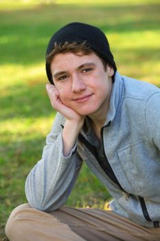 Grinning male teen with hand on chin sitting outdoors