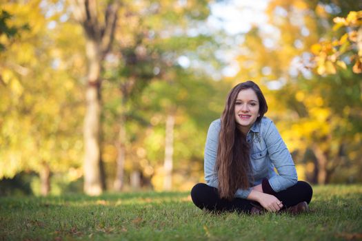Cheerful single female teenager sitting outdoors on grass