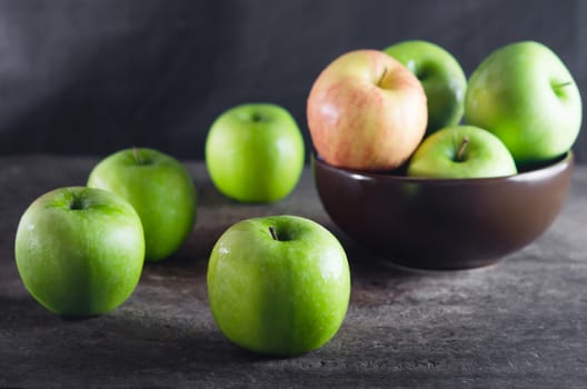 Bowl of green apples and apple over wooden board