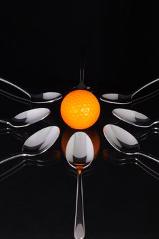 Teaspoons and orange golf ball on the black glass desk