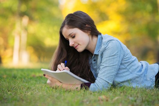 Grinning young woman writing on notebook outdoors