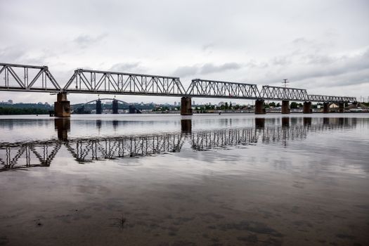 Petrivskiy railroad bridge in Kyiv (Ukraine) across the Dnieper shot from the left bank of the river on the cloudy day,
