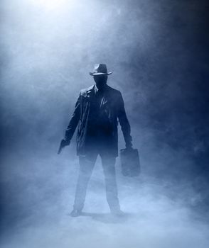 Faceles man with a gun and a briefcase standing in the fog.