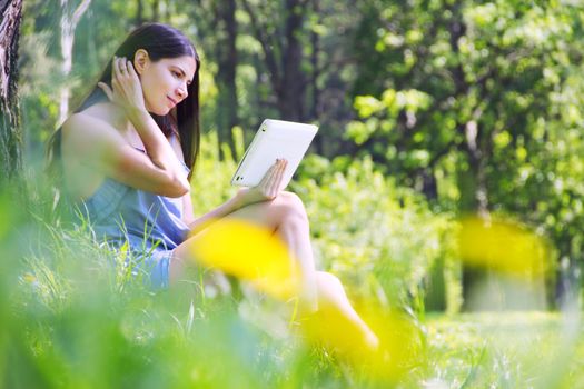 Young woman using tablet outdoor sitting green grass with flowers