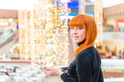 smiling girl with the phone and coffee in the mall