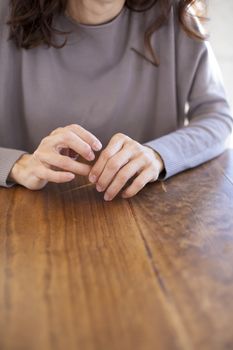 hands of brunette woman with mauve color sweater on light brown wooden table