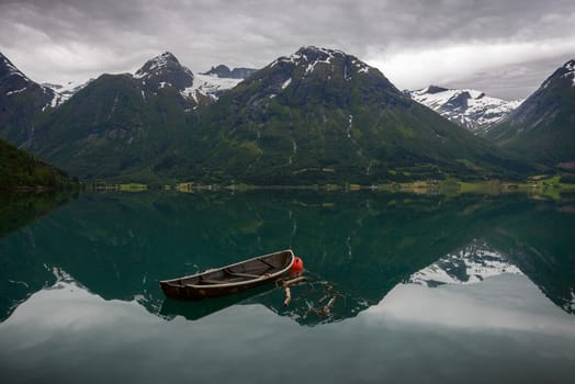 An old row boat in the still water of Oppstrynsvatnet with reflection of the mountains in a Norwegian landscape at Hjelle, Sogn og Fjordane, Norway.