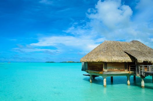 Luxury thatched roof honeymoon bungalow in a vacation resort in the clear blue lagoon of the tropical island of Bora Bora, near Tahiti, in French Polynesia.