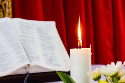 bible open on a table with candle and red curtain as background. flower as foreground. Perfect for religion, easter and christmas themes. candle fucused