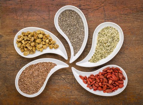 superfood samples  (mulberry, chia seeds, hemp seeds, goji berry, flax seed) in teardrop shaped bowls against grunge wood