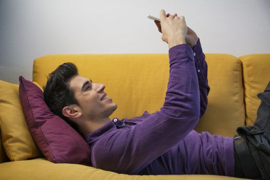 Sexy handsome young man sitting indoors posing for a selfie on his mobile phone smiling for the camera