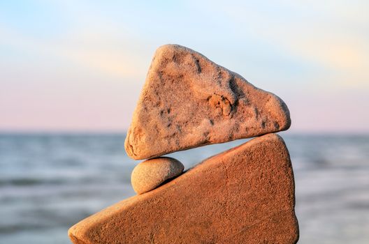 Balancing of round pebble between triangle stones on the seashore