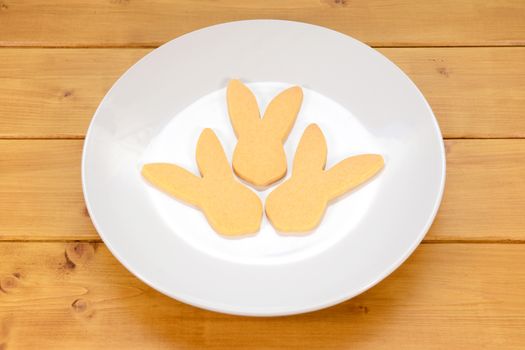 Three rabbit-shaped biscuits for Easter on a white plate on a wooden table