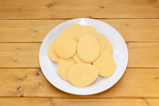 Pile of egg-shaped biscuits for Easter on a white plate on a wooden table