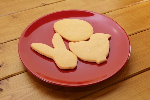 Cookies in egg, chick and rabbit shapes for Easter on a red plate on a wooden table