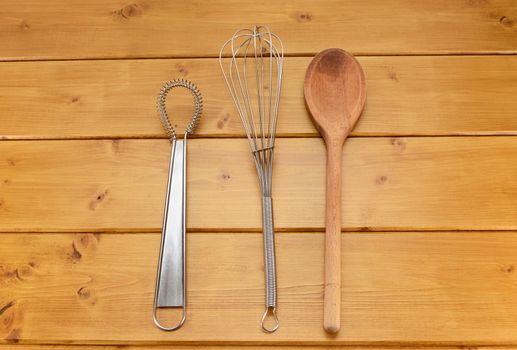 Sauce and balloon whisks and wooden spoon on a kitchen table
