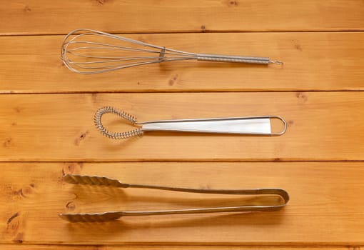 Balloon and sauce whisks and metal tongs on a wooden table