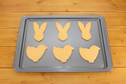 Baking tray with six Easter cookies - bunnies and chicks - on a wooden table