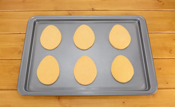 Six egg shaped Easter cookies on a baking tray on a wooden table
