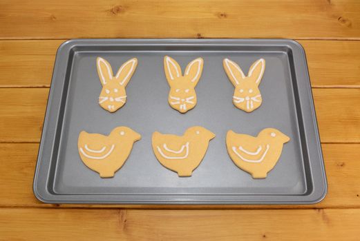 Iced Easter biscuits in bunny and chick shapes on a baking tray on a kitchen table