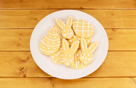 Plate full of frosted Easter cookies on a wooden table - egg and bunny shapes