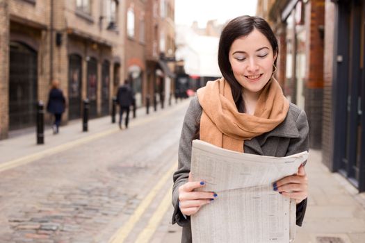 young woman reading her paper in the street