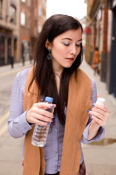 young woman holding her pills and a bottle of water in the street