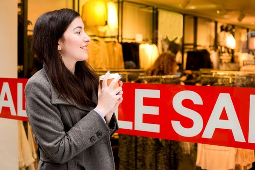 young woman looking in a shop window with a coffee