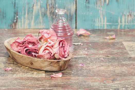 Essential oil with roses on rustic wooden background. A macro photograph with shallow depth of field. Done with a vintage retro filter