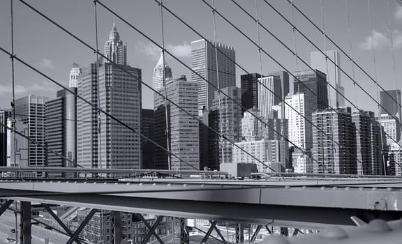 Black and white New York City skyscrapers seen through the wires of the Brooklyn Bridge.