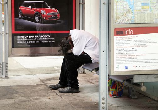 San Francisco, California, USA - August 15, 2013: Homeless man sleeping on a bench at a bus stop in San Francisco