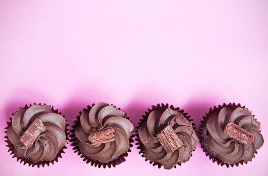 Chocolate cupcakes creating a border over a pink background
