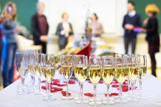 Banquet event. Waiter pouring champagne into glass. Table with the wineglasses, snacks and cocktails.