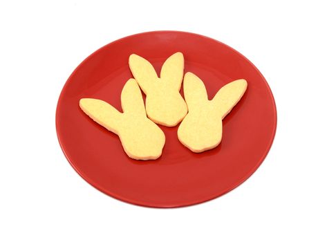 Three rabbit-shaped cookies for Easter on a red plate, isolated on a white background