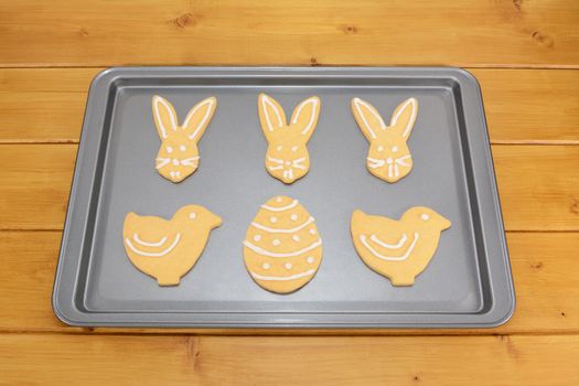 Easter cookies decorated with white frosting on a baking tray on a wooden table