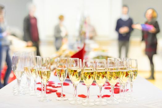 Banquet event. Table with the wineglasses, snacks and cocktails. People celebrating in the background.