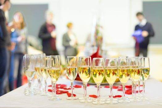 Banquet event. Table with the wineglasses, snacks and cocktails. People celebrating in the background.