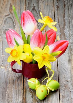 Bunch with Yellow Daffodils and Magenta Tulips in Watering Can with Colored Easter Eggs closeup on Wooden background