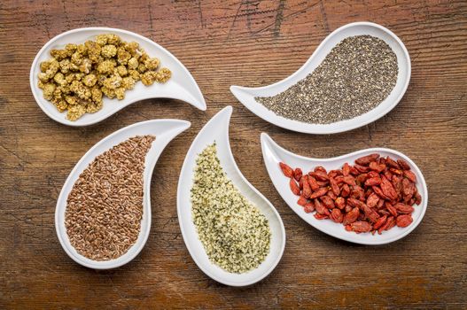 superfood samples  (mulberry, chia seeds, hemp seeds, goji berry, flax seed) in teardrop shaped bowls against grunge wood