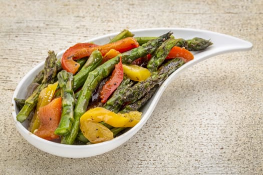 roasted asparagus salad with bell pepper on a teardrop shaped bowl against white painted rustic wood