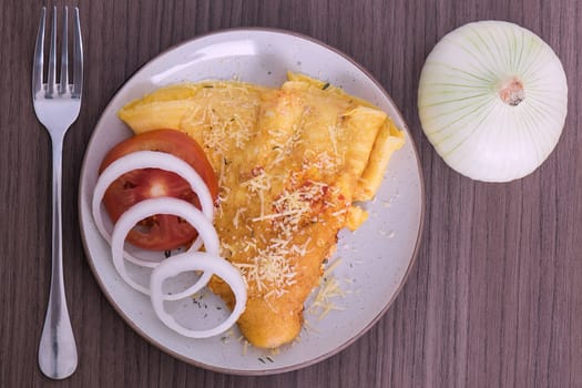 Overhead view of a dish of omelette with parmesan cheese, a fork and an onion