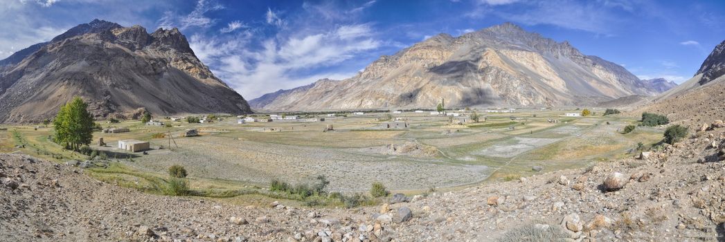 Scenic panorama of small remote village with grain fields in Tajikistan on sunny day