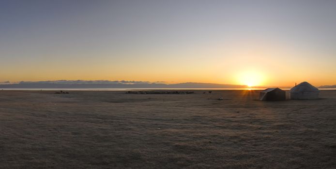 Scenic panorama of sunset on green grasslands in Kyrgyzstan with traditional nomadic yurt